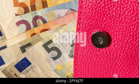 Banconote in euro. Moneta europea su sfondo bianco. Una borsa o una borsa di colore rosa brillante con un bottone di metallo, da cui il denaro viene distribuito in un ventilatore. Banconote da 5, 10, 20, 50 e 100 Foto Stock