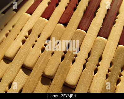 tappetino in legno o lamellare. Il tappeto è un tappetino sotto il caldo. Bastoncini di legno lavorato a maglia con bordi arrotondati. Primo piano. Colori giallo, marrone e beige. Illuminazione laterale. Consistenza tradizionale del tampone di bambù Foto Stock