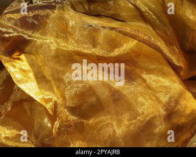 L'organza è giallo-marrone con una lucentezza beige. Tessuto lucido, riflettente, bellissimo per tende e tulle. Opzione di design degli interni. Sezione di organza ritorta e ripiegata casualmente alla luce del sole Foto Stock