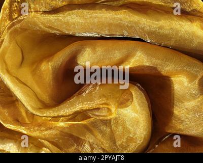 L'organza è giallo-marrone con una lucentezza beige. Tessuto lucido, riflettente, bellissimo per tende e tulle. Opzione di design degli interni. Sezione di organza ritorta e ripiegata casualmente alla luce del sole Foto Stock