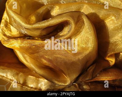 L'organza è giallo-marrone con una lucentezza beige. Tessuto lucido, riflettente, bellissimo per tende e tulle. Opzione di design degli interni. Sezione di organza ritorta e ripiegata casualmente alla luce del sole Foto Stock