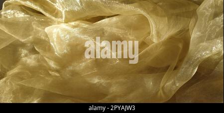 L'organza è giallo-marrone con una lucentezza beige. Tessuto lucido, riflettente, bellissimo per tende e tulle. Opzione di design degli interni. Sezione di organza ritorta e ripiegata casualmente alla luce del sole Foto Stock