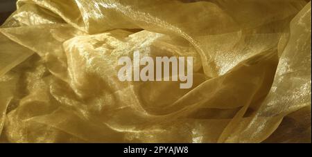 L'organza è giallo-marrone con una lucentezza beige. Tessuto lucido, riflettente, bellissimo per tende e tulle. Opzione di design degli interni. Sezione di organza ritorta e ripiegata casualmente alla luce del sole Foto Stock