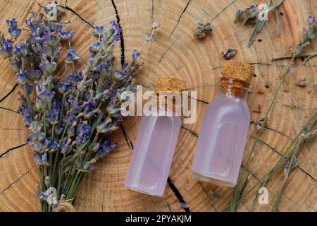 Bella lavanda fiori e bottiglie di olio essenziale su ceppo di legno, piatto Foto Stock