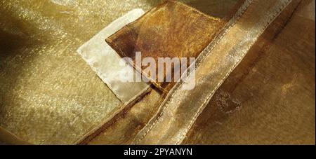 Anelli per tende. Splendido tessuto dorato. Organza nelle tonalità giallo, arancione, beige e marrone. Pieghe nel tessuto. Gradiente luminoso sotto la luce. Tulle di seta piegato. Materiale per tende trasparente. Banner Foto Stock