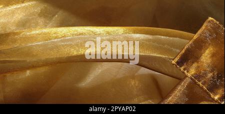 Splendido tessuto dorato. Organza nelle tonalità giallo, arancione, beige e marrone. Pieghe nel tessuto. Gradiente luminoso sotto la luce. Tulle di seta piegato. Materiale per tende trasparente Foto Stock