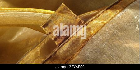 Anelli per tende. Splendido tessuto dorato. Organza nelle tonalità giallo, arancione, beige e marrone. Pieghe nel tessuto. Gradiente luminoso sotto la luce. Tulle di seta piegato. Materiale per tende trasparente Foto Stock