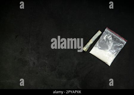 Linee di polvere di cocaina, banconote arrotolate e farmaci in tasca in busta di plastica su fondo in vetro nero, vista dall'alto. Concetto di tossicodipendenza Foto Stock