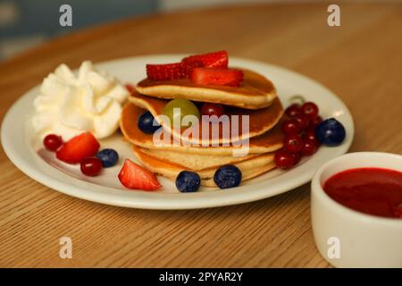 Gustose frittelle con frutti di bosco freschi e panna montata su un tavolo di legno Foto Stock