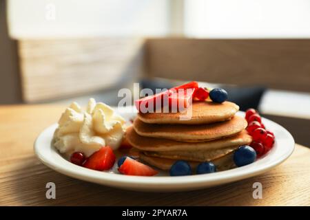 Gustose frittelle con frutti di bosco freschi e panna montata su un tavolo di legno Foto Stock