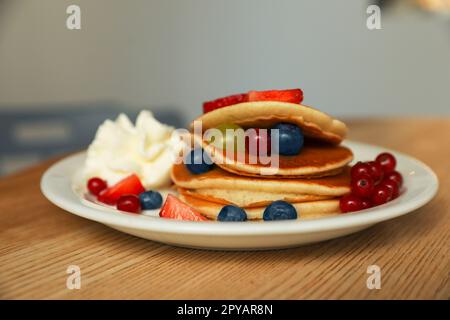 Gustose frittelle con frutti di bosco freschi e panna montata su un tavolo di legno Foto Stock