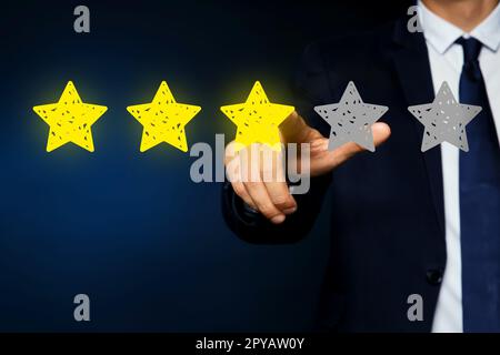 Uomo che indica icone di stelle su sfondo blu scuro, primo piano. Valutazione della qualità Foto Stock