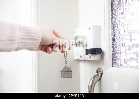 Donna che mette la chiave della casa nella serratura della porta principale della casa, donna che usa una chiave argentata per aprire la serratura della porta principale, porta di legno bianca aperta casa chiusa a chiave, sicurezza e salvare Foto Stock