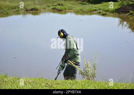 Uomo in un campionato di detettorismo utilizzando un metal detector su un lotto erboso con un lago sullo sfondo. Concorso hobby per trovare premi. Tesoro hu Foto Stock
