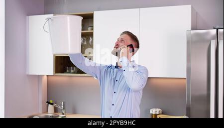 Uomo che chiama l'idraulico mentre raccoglie le perdite d'acqua dal soffitto Foto Stock