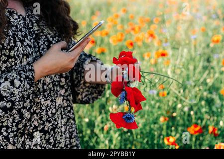 Donna più foto di formato utilizzando un telefono wreath di fiori selvatici: Papaveri rossi e fiori di mais blu Foto Stock