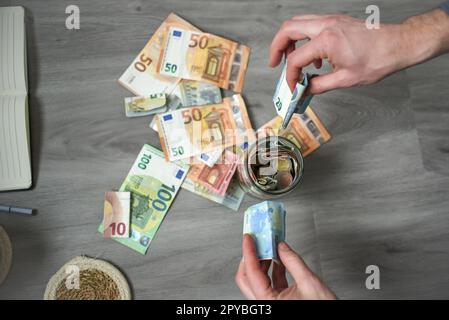 Le mani di un uomo contano le banconote in euro in ufficio, mettendo i soldi in un barattolo di risparmio Foto Stock