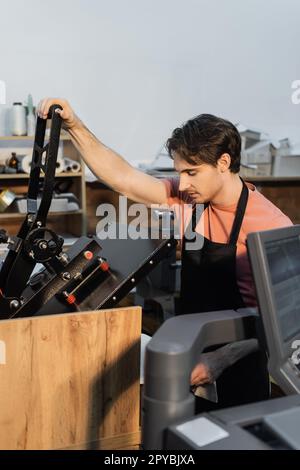 uomo in grembiule che utilizza un plotter di stampa professionale mentre lavora nel centro di stampa, immagine stock Foto Stock