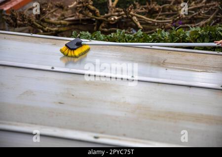 Lavaggio del copricapo pergolato in alluminio. rimuovere le alghe sporche con sapone a spazzola e acqua vicino in giardino da una terrazza casa Foto Stock