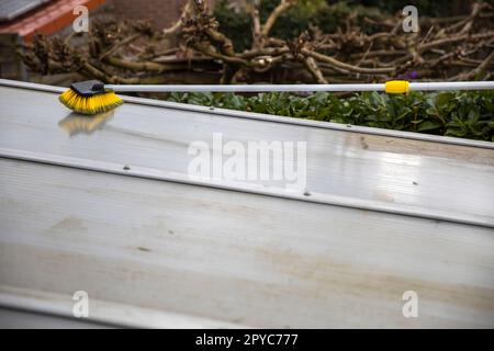 Lavaggio del copricapo pergolato in alluminio. rimuovere le alghe sporche con sapone a spazzola e acqua vicino in giardino da una terrazza casa Foto Stock