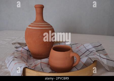 Vecchia caraffa in ceramica non dipinta in un vassoio su una tovaglia tradizionale. Argilla decorazione oggetti concetto foto idea. Foto Stock