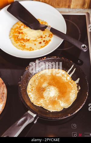 Preparazione di pancake sottili su padella in cucina, con impasto da cuocere per crepes e pancake Foto Stock