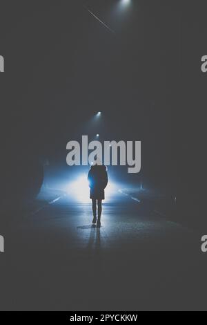 Strada oscura con una donna che cammina nel mezzo. ragazza solitaria donna in piedi al buio parcheggio al buio di notte vicino a stop strada segnaletica no drive pensare soffrire stress depressione disperazione (immagine colorata) Foto Stock