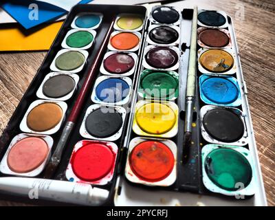 Una serie di acquerelli di colori diversi per il disegno. Contenitori rotondi multicolori con vernice lucida. Strumenti per la lezione di disegno e manodopera. Carta colorata. Rosso, blu, giallo, verde. Foto Stock