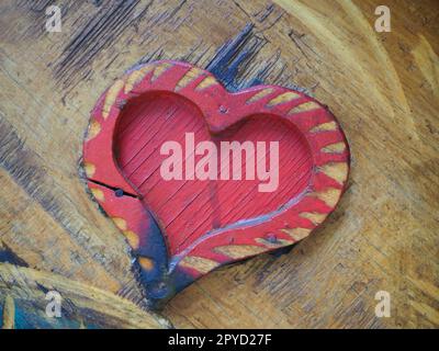 Forma a cuore di falegnameria su una superficie di legno e verniciata di rosso. Un simbolo di amore e fedeltà. Cartolina per le congratulazioni o il riconoscimento di San Valentino. Segni di influenza dell'accensione o dell'umidità. Foto Stock