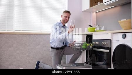 Giovane che prende il bicchiere da bere dalla lavastoviglie Foto Stock