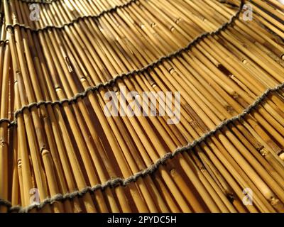 Una biancheria da letto in paglia, una tovaglia o un piccolo tappeto appoggiato su un tavolo e fotografato lateralmente. La luce del sole della sera si riflette sui gambi. Alcuni bastoncini sono rotti, fili e funi sono intrecciati Foto Stock