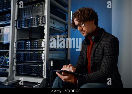 Giovane uomo hipster che utilizza un tablet digitale che lavora nella sala server Foto Stock