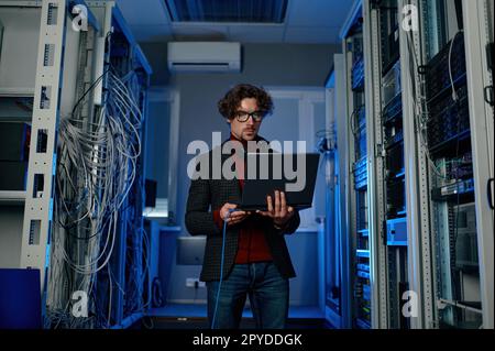 Uomo ESPERTO IT con un notebook che lavora all'aggiornamento del software del data center Foto Stock