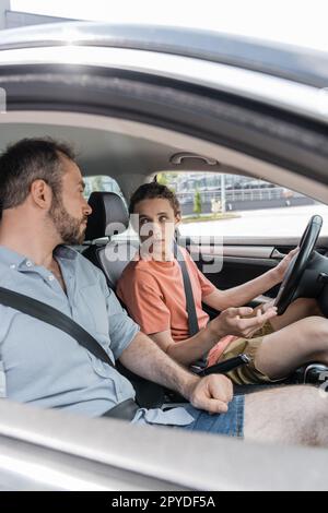 ragazzo felice adolescente che parla con il padre, mentre imparando a guidare l'auto, immagine stock Foto Stock