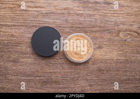 Contenitore di polvere minerale sfuso per la tonalità della pelle su sfondo di legno, vista dall'alto ravvicinata Foto Stock