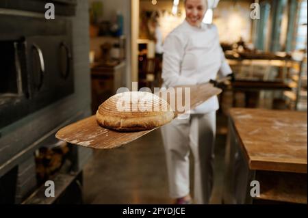 Giovane lavoratore di panetteria usando pala di legno per prendere il pane dal forno di stufa Foto Stock