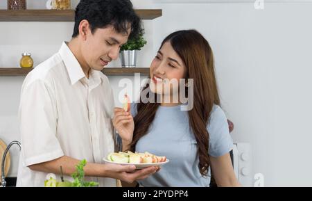 Coppie asiatiche trascorrono del tempo insieme in cucina. Giovane donna nutrire il suo ragazzo un pezzo di mela. Foto Stock