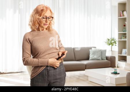 Donna matura che inietta insulina sparata nella pancia a casa in un salotto Foto Stock