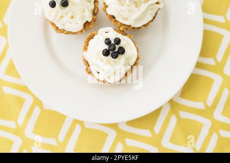 Muffin fatti in casa con mirtilli, panna e frutti di bosco freschi su un tovagliolo giallo Foto Stock