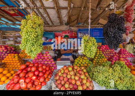 Bangladesh, Khulna, venditore di frutta sul mercato che vende uva, mele e agrumi. Gennaio 30, 2012. Solo per uso editoriale. Foto Stock