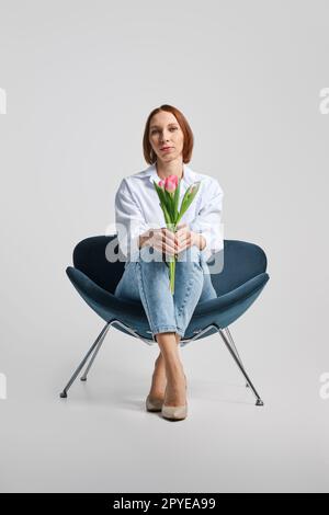 Vista dall'angolo basso con una donna positiva di mezza età seduta in poltrona con tulipani Foto Stock