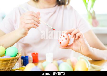 Primo piano delle mani femminili che tengono un uovo di Pasqua e dipingono con un pennello. Preparazione alla Pasqua Foto Stock