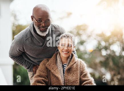 Spingendo attraverso il dolore. un uomo anziano che spinge la moglie in sedia a rotelle intorno al cortile a casa. Foto Stock