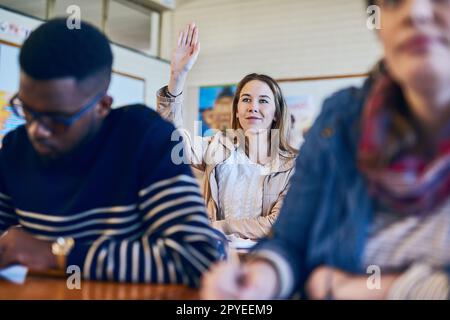 Conosco la risposta. una giovane donna che alza la mano in classe. Foto Stock