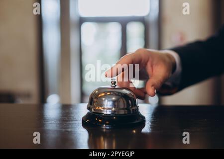 Arrivo in hotel. Un uomo suona un campanello di servizio alla reception per attirare l'attenzione. Foto Stock