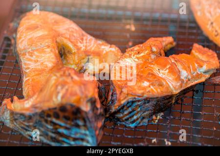 Salmone affumicato caldo. Grandi pezzi di salmone dell'Atlantico sono affumicati su una griglia affumicata da vicino. Pianta di fumo di pesce. Foto Stock