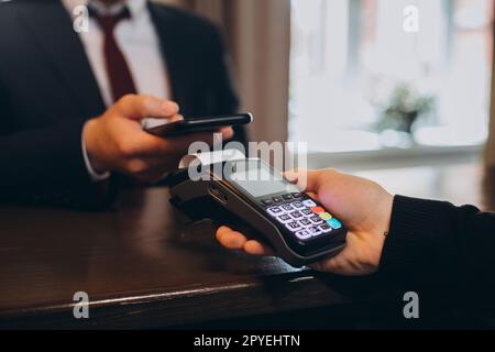 Un uomo d'affari paga un conto per una camera d'albergo attraverso uno smartphone che utilizza la tecnologia NFC. Foto Stock