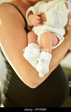 I calzini corrispondono al suo vestito. un ragazzino irriconoscibile che dorme mentre sua madre lo tiene in mano a casa. Foto Stock