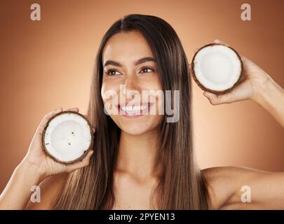 Donna, cura della pelle e cocco in studio, felice o sorriso per la cura di sé, nutrizione o salute cosmetica. Modello, benessere della pelle e frutta per olio, idratante o cosmetici sfondo per un'illuminazione naturale e radiosa Foto Stock