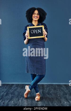 Tutti i clienti Benvenuto. Foto studio di una giovane donna che tiene una lavagna con la parola aperta su di essa su uno sfondo blu. Foto Stock